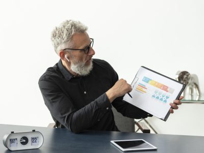 older-man-home-showing-graph-notepad-with-tablet-desk